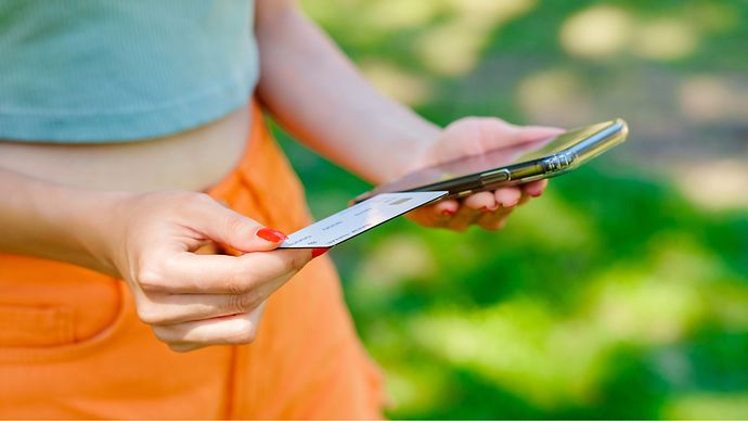 weibliche Hände halten ein Handy und eine Scheckkarte