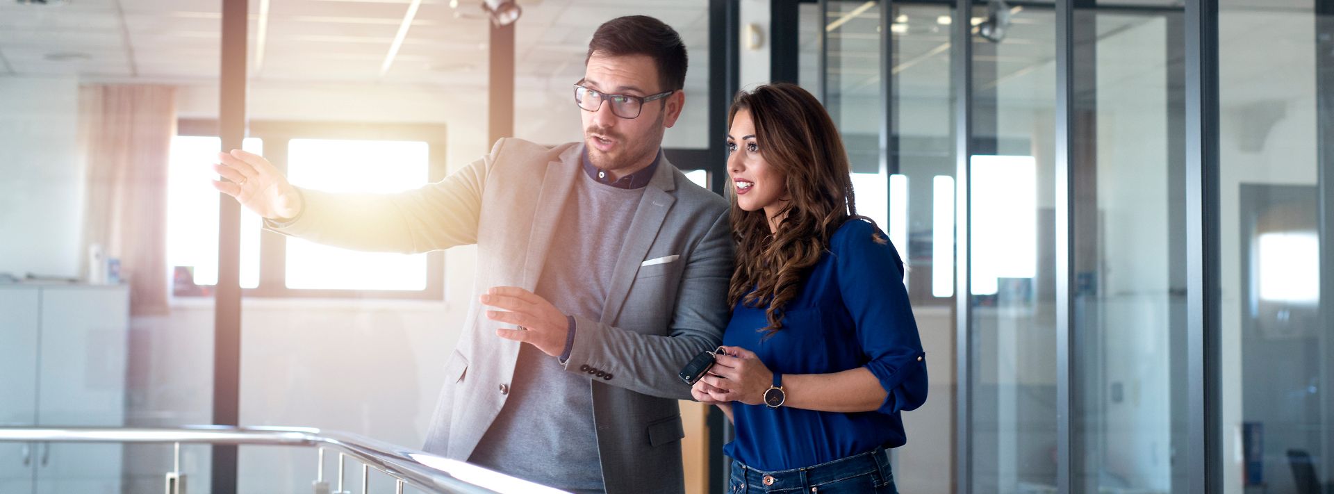 © stock.adobe.com/littlewolf1989 Ein Mann und eine Frau stehen in einem modernen Büro und diskutieren etwas, während der Mann auf etwas zeigt.
