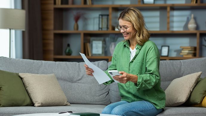Eine Frau sitzt einen Brief und Taschenrechner in der Hand haltend auf einem Sofa