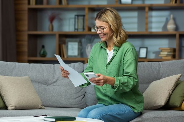 Eine Frau sitzt einen Brief und Taschenrechner in der Hand haltend auf einem Sofa