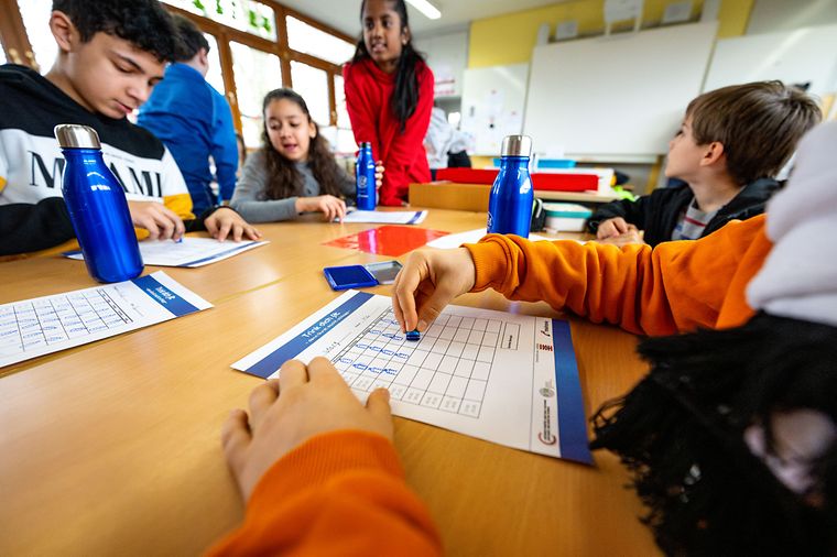 © Florian Wiegand Kinder sitzen an einem Gruppentisch in der Schule, mit blauen Trinkflaschen und Arbeitsblättern