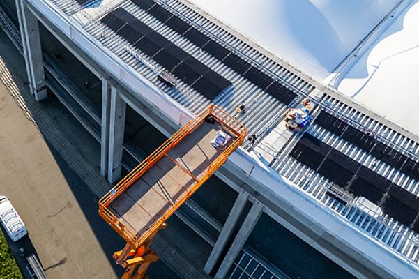 Eine Hebebühne hebt Arbeiter auf ein Dach, wo Solarpaneele installiert werden.