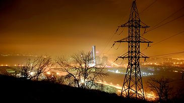 Strommast bei Nacht im Hintergrund beleuchtete Skyline