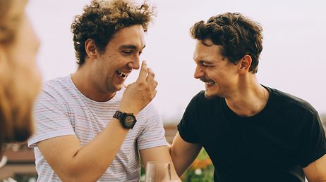 Zwei glückliche Männer auf einer Dachterasse lachen zusammen