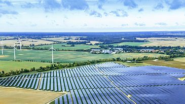 Großer Solarpark mit Windrädern in weiter Landschaft – Symbol für erneuerbare Energie und nachhaltige Stromerzeugung.