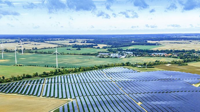 Großer Solarpark mit Windrädern in weiter Landschaft – Symbol für erneuerbare Energie und nachhaltige Stromerzeugung.