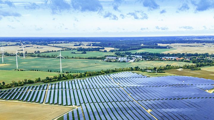 Großer Solarpark mit Windrädern in weiter Landschaft – Symbol für erneuerbare Energie und nachhaltige Stromerzeugung.