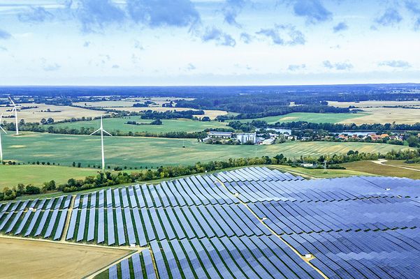 Großer Solarpark mit Windrädern in weiter Landschaft – Symbol für erneuerbare Energie und nachhaltige Stromerzeugung.