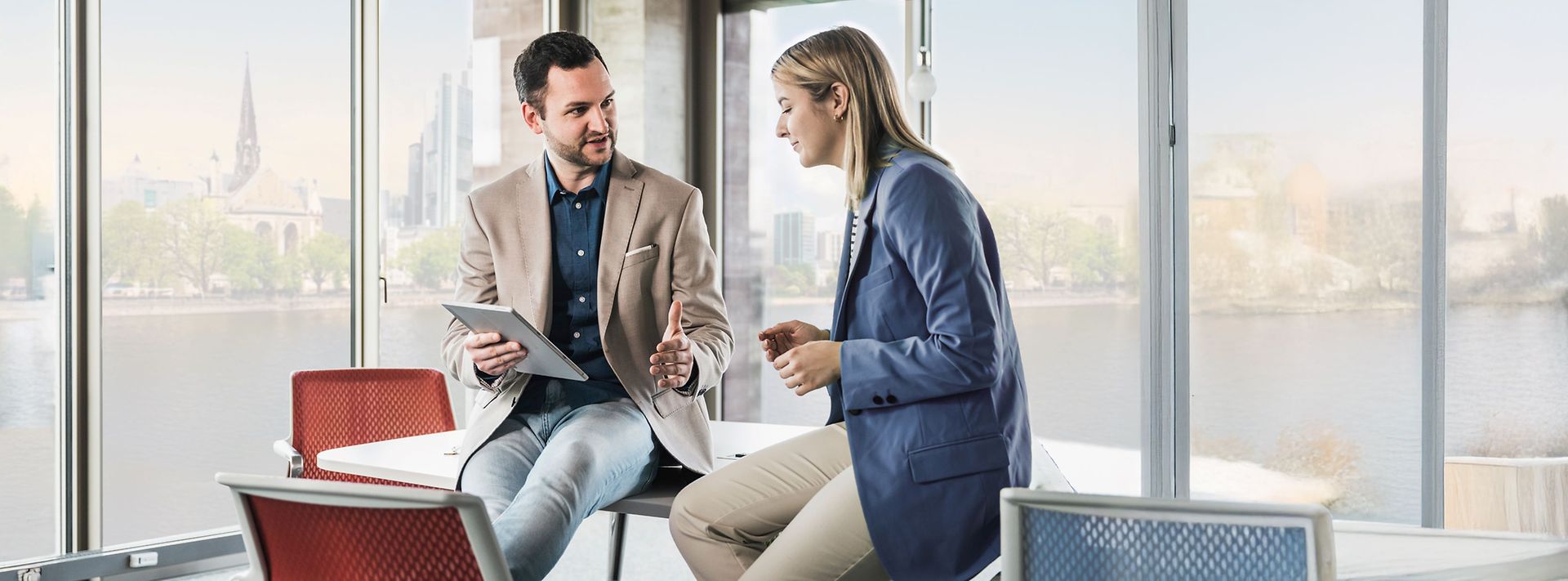 Geschäftsmeeting zwischen Mann und Frau im Büro vor der Skyline Frankfurt.