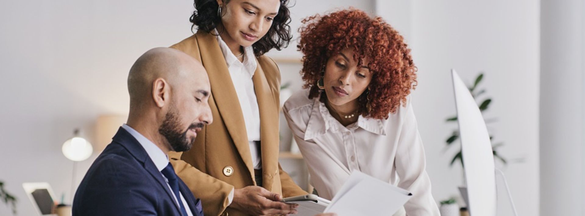 © www.istock.com - LumiNola Ein Mann sitzt am Schreibtisch und hat Papiere vor sich, zwei Frauen beugen sich darüber