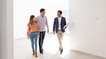 Immobilienmakler führt ein junges Paar durch eine leer stehende Wohnung