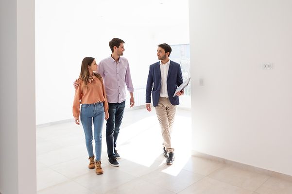 Immobilienmakler führt ein junges Paar durch eine leer stehende Wohnung