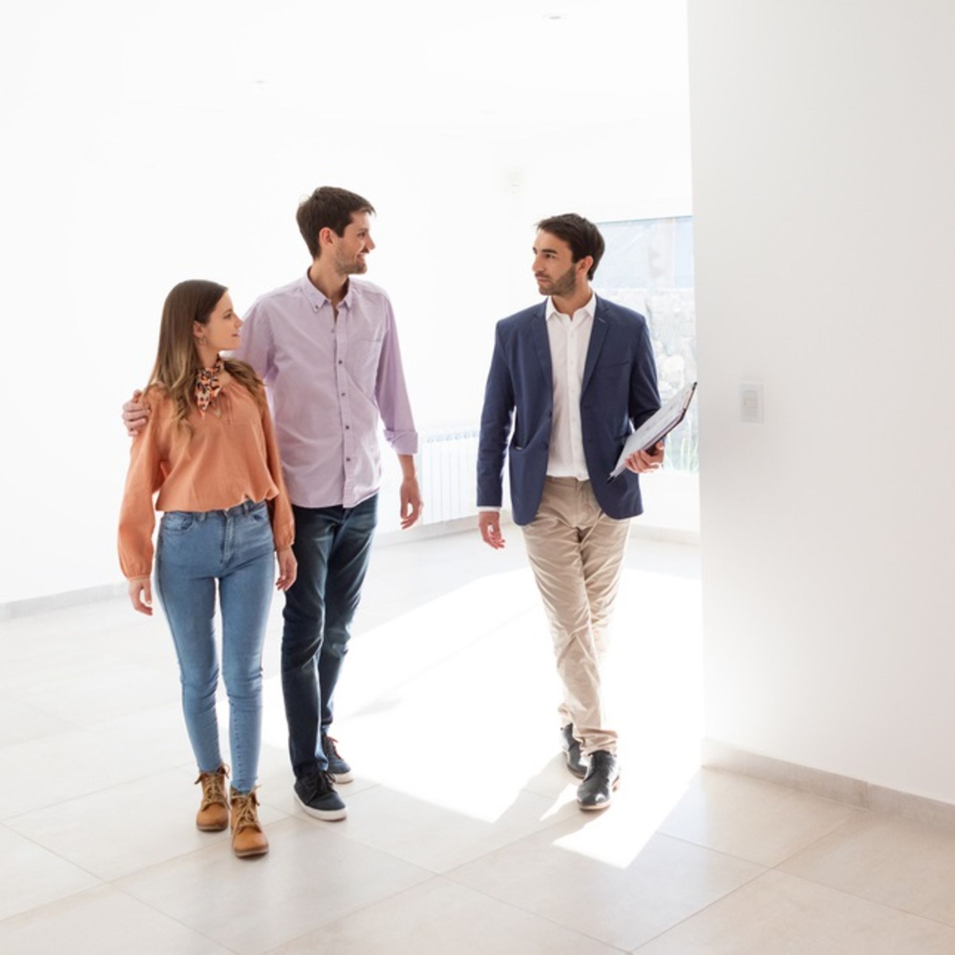 Immobilienmakler führt ein junges Paar durch eine leer stehende Wohnung