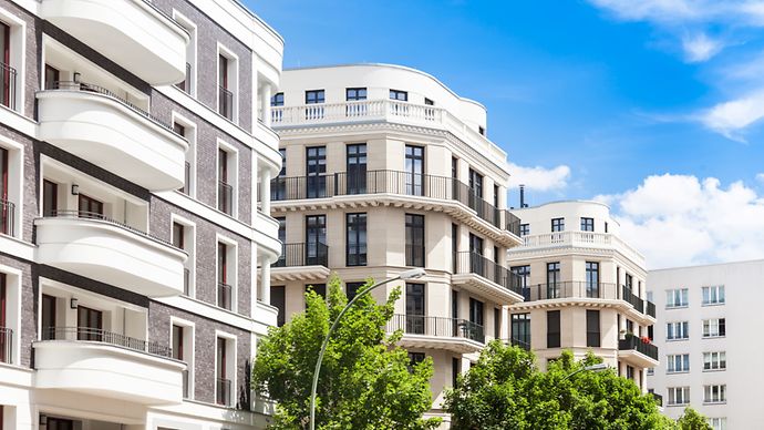 Moderne Wohngebäude mit Balkonen und großen Fenstern, umgeben von Bäumen unter einem blauen Himmel mit weißen Wolken.