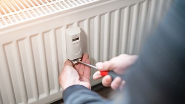 Zwei Hände, die mit einem Schraubendreher einen Heizkostenverteiler am Heizkörper befestigen