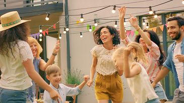 Gruppe tanzt im Garten unter Lichterkette, bunte Wimpel hängen vor einem Wohnhaus.