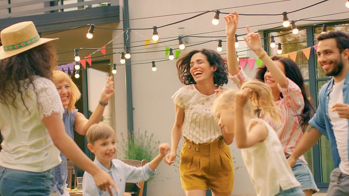 Gruppe tanzt im Garten unter Lichterkette, bunte Wimpel hängen vor einem Wohnhaus.