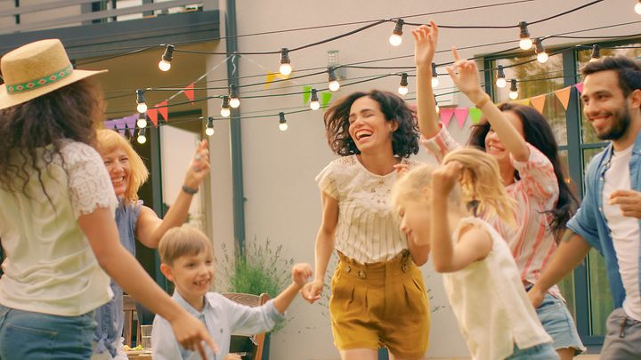 Gruppe tanzt im Garten unter Lichterkette, bunte Wimpel hängen vor einem Wohnhaus.