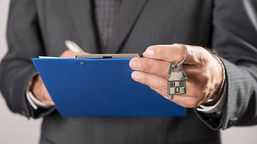 Eine Hand hält ein Übergabeprotokoll, die andere Hand einen Hausschlüssel