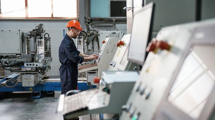 Blick von der Seite, Arbeiten mit Maschine, Bediener. Fabrikarbeiter ist mit Schutzhelm drinnen