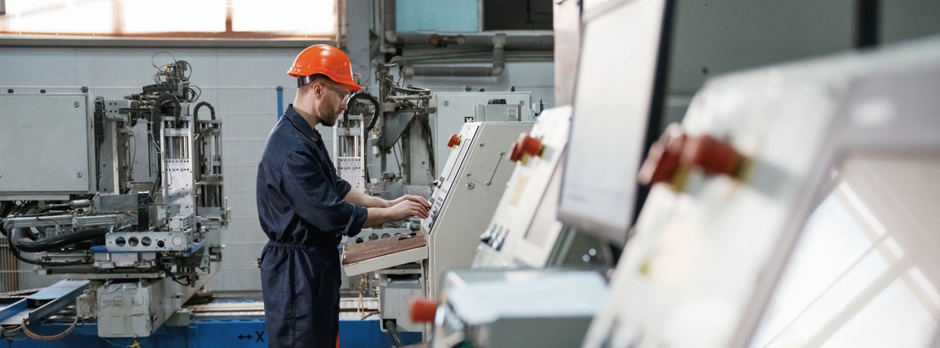 Blick von der Seite, Arbeiten mit Maschine, Bediener. Fabrikarbeiter ist mit Schutzhelm drinnen