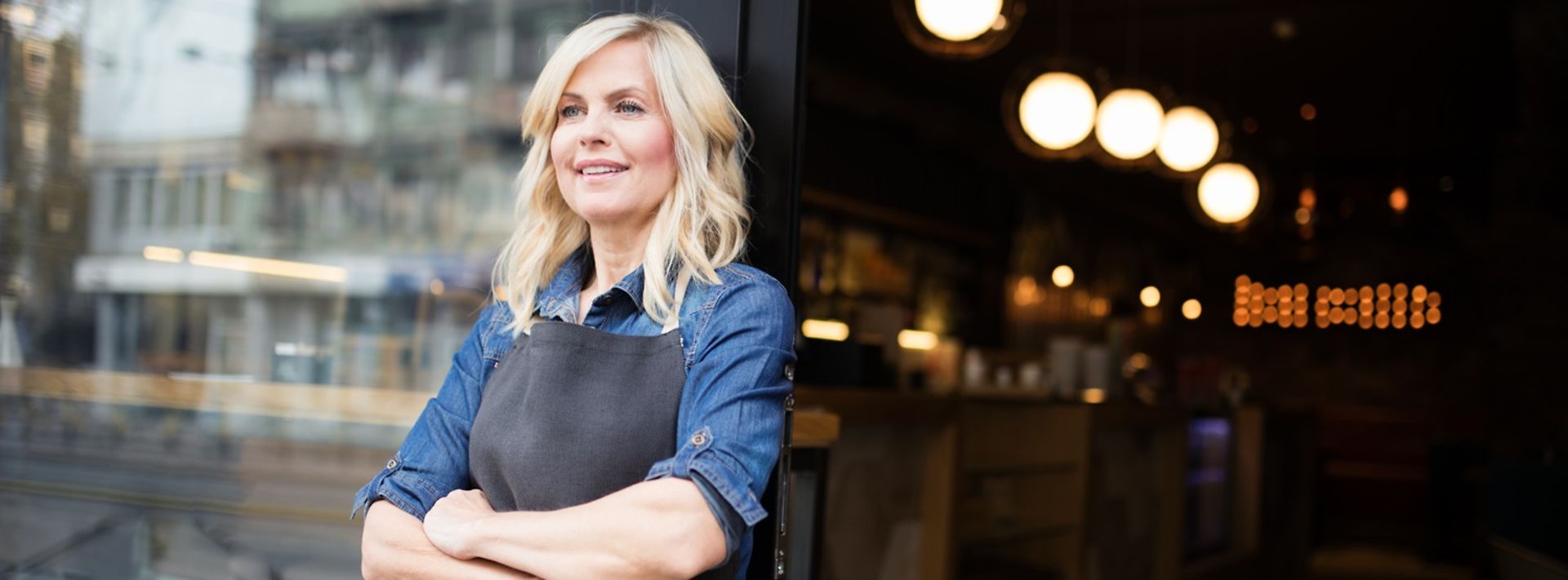 Wirtin seht lächelnd vor ihrem Restaurant, dahinter leuchten die Deckenlampen