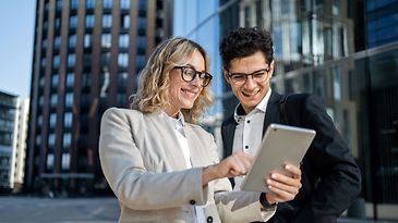Frau und Mann mittleren Alters schauen auf ein Tablet und lachen