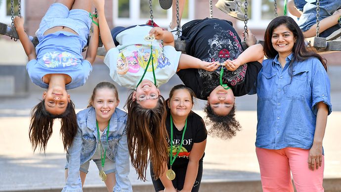 5 Kinder und ein Erwachsener posieren auf einem Spielplatz mit ihren Medallien 