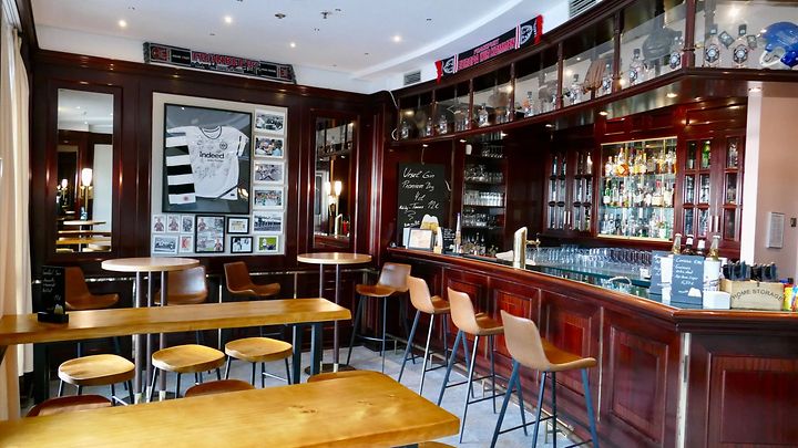 Gemütliche Sportsbar mit Holztheke, Barhockern, Tischen und dunklen Holzwänden.