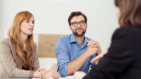 Zwei Personen hören einer dritten zu, Mann nickt zustimmend.