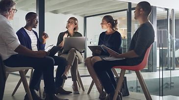Fünf Personen mit Laptops sitzen in einem Stuhlkreis und unterhalten sich