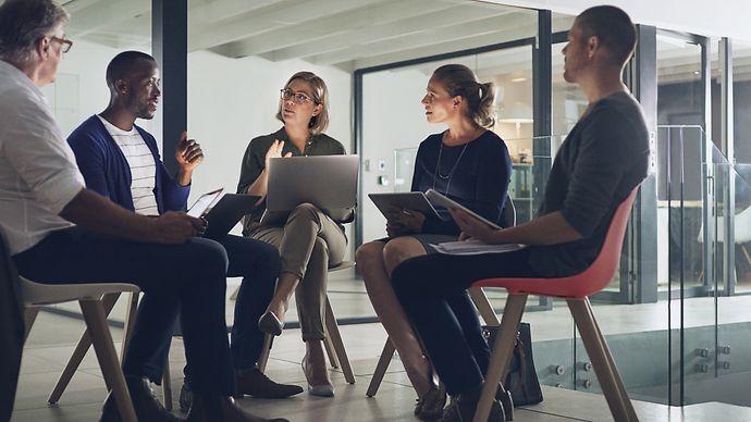 Fünf Personen mit Laptops sitzen in einem Stuhlkreis und unterhalten sich