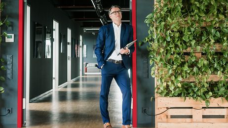 Geschäftsmann lehnt in Gebäudeeingang, links und rechts von ihm ranken sich Grünpflanzen an den Wänden