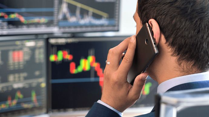 Mann am Handy vor Bildschirmen