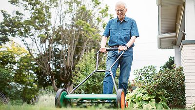 Ein älterer Mann schiebt einen mechanischen Handräsenmäher über Rasen