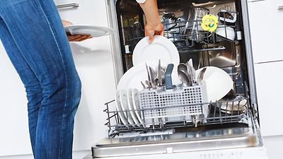 Frau räumt Geschirr in Geschirrspüler