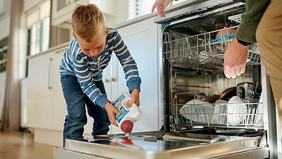 Junge schüttet Geschirrspüler in die Spülmaschine