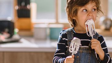 Kleiner Junge in einer Küche leckt Schlagsahne von Rührstäben ab