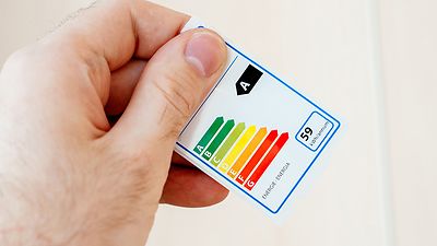 Hand hält Energielabel mit den Energieeffizienzklassen als Pfeildiagramm, von A (grüner Pfeil) bis G (roter Pfeil)
