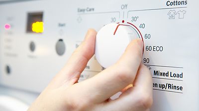Hand stellt Temperatur an der Waschmaschine auf 30 Grad ein