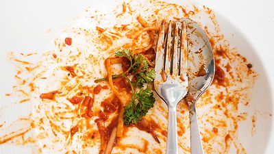 Teller mit Gabel und Löffel sowie Resten von roter Sauce, Nudeln und Petersilie