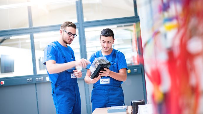 Zwei Jugendliche im Blaumann schauen sich einen kleinen Elektrobox an.
