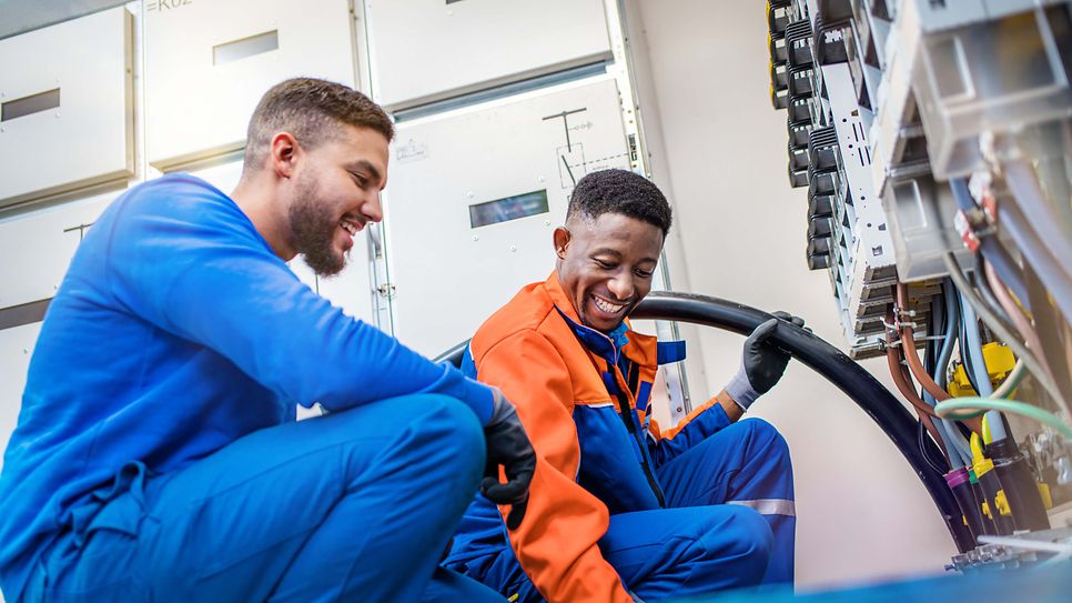 Zwei Techniker verlegen am Schaltkasten eine Starkstromleitung