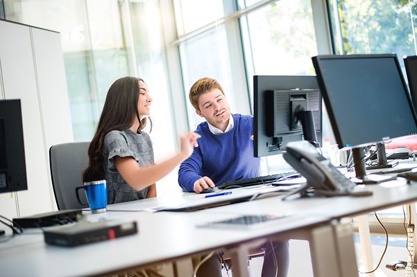 Zwei Studierende sitzen gemeinsam am Computermonitor und besprechen sich