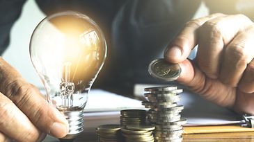 © stock.adobe.com/mintra Mann hält Glühbirne und zählt Münzgeld