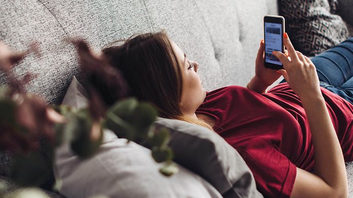 Frau liegt mit Handy auf dem Sofa und nutzt Service-Angebot