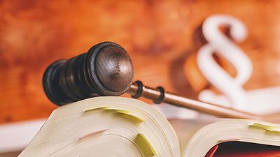 Ein aufgeschlagenes Buch mit farbigen Markierungen, im Hintergrund liegt ein Richterhammer.