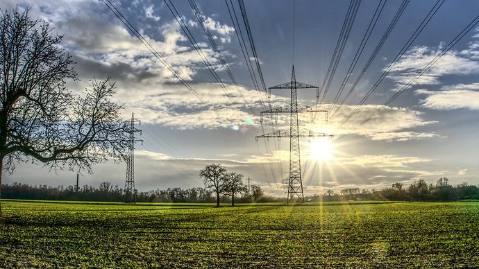 Freileitungsmasten auf einem Feld, Sonne strahlt am Himmel