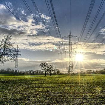 Freileitungsmasten auf einem Feld, Sonne strahlt am Himmel