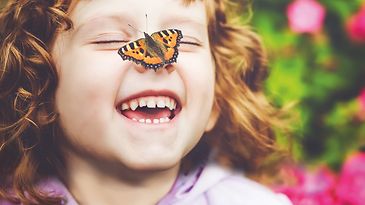 Schwarz-orange gemusterter Schmetterling landet auf der Nase eines kleinen Mädchens, welches lacht.